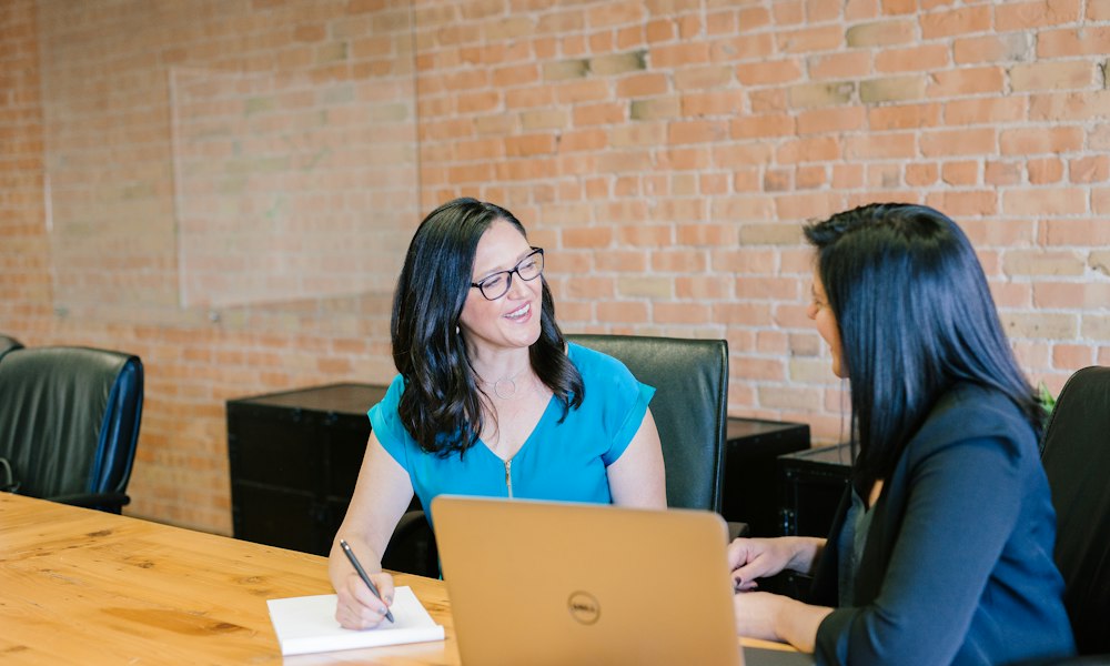 Woman in teal shirt beside a woman in a suit jacket
